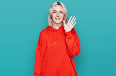 Genç sarışın kız gündelik giysiler giyer ve beş numarayı göstererek gülümserken kendinden emin ve mutluydu.. 