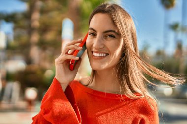 Genç İspanyol kadın gülümsüyor. Şehirdeki akıllı telefondan konuşuyor..