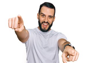 Sakallı, günlük beyaz tişörtlü genç adam seni ve kamerayı işaret ediyor. 