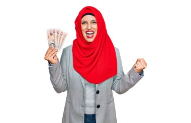 İslami tesettürlü güzel İspanyol kadın elinde 5 kilo banknotla gururla bağırıyor, zaferi kutluyor ve başarıyı kollarını kaldırarak kutluyor. 