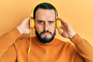 Sakallı genç adam kulaklık takıyor şüpheci ve gergin, sorun yüzünden surat asıyor. negatif kişi. 