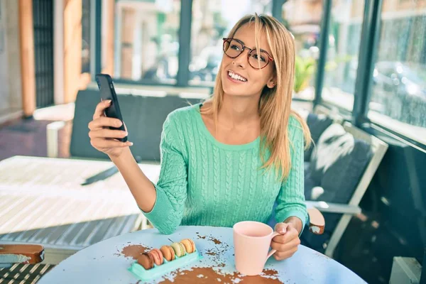 若いですブロンド女性を使用してスマートフォンやコーヒーショップテラスでコーヒーを飲む — ストック写真