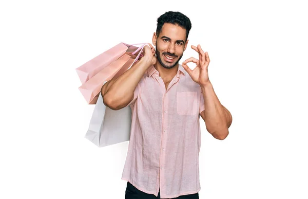 留着胡子的西班牙男人拿着购物袋 手拿着手签 微笑着表示友善的手势 是个很好的象征 — 图库照片