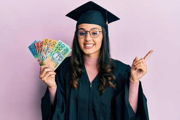 Young Hispanic Woman Wearing Graduation Uniform Holding Australian Dollars Smiling — Stock Photo, Image