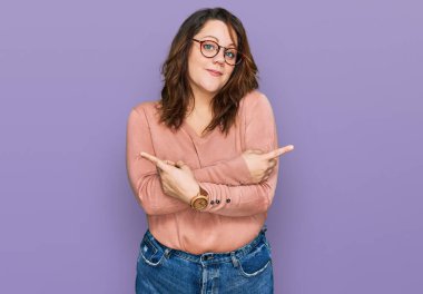 Gündelik kıyafet giyen ve gözlük takan genç ve cüsseli bir kadın her iki tarafı da parmaklarıyla işaret ediyor. Farklı yönlere bakıyor. 