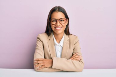 Ofiste çalışan güzel İspanyol kadın kollarını kavuşturup kameraya bakarak gülümsüyor. pozitif kişi. 