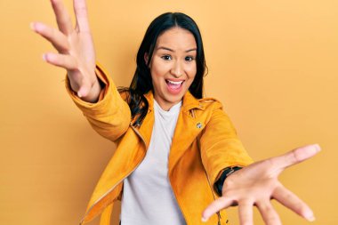 Sarı deri ceketli, burun piercingli güzel İspanyol kadın sarılmak için kollarını açmış kameraya bakıyor. Mutluluğu kucaklayan neşeli bir ifade.. 