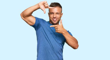 Yakışıklı, sıradan kıyafetler giyen, gülümseyen, elleri ve parmakları gülen yüzlü kaslı bir adam. yaratıcılık ve fotoğrafçılık kavramı. 