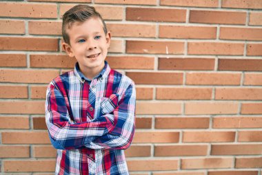 Kollarını kavuşturup gülümseyen sevimli beyaz çocuk şehrin duvarına yaslanmış mutlu..