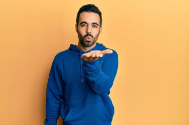 Gündelik giysiler giymiş genç İspanyol bir adam kameraya bakıp havada bir öpücük savuruyor ve sevimli ve seksi oluyor. aşk ifadesi. 