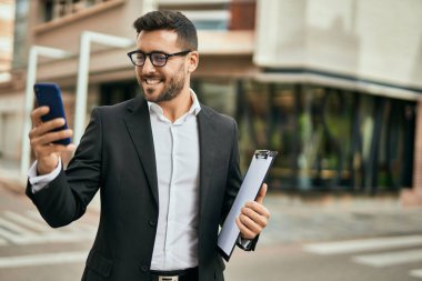 Genç İspanyol işadamı şehirde akıllı telefon kullanarak mutlu bir şekilde gülümsüyor..