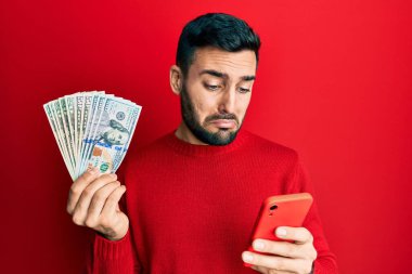 Genç İspanyol adam, elinde dolarları tutan akıllı telefon kullanıyor. Depresyonda ve endişe içinde, sinirli ve korkmuş. hüzünlü ifade. 