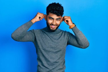 Balıkçı yaka kazak giyen sakallı, kulakları parmaklarıyla çeken Arap bir adam. Komik bir jest. deneme sorunu 