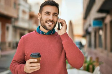 Genç İspanyol adam akıllı telefondan konuşuyor. Şehirde kahve içiyor..