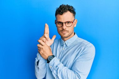 Gündelik kıyafetler ve gözlük takan genç İspanyol adam sembolik bir silah tutuyor. El hareketleriyle cinayet silahlarıyla oynuyor. Kızgın surat. 