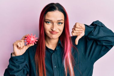 Kafkasyalı genç bir kadın elinde kızgın suratlı bir virüs oyuncağı tutuyor. Negatif işaretler baş parmakları aşağıda, reddedilme konsepti ise... 