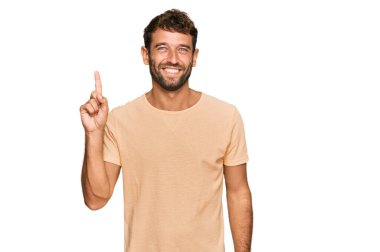 Sıradan tişörtler giyen sakallı yakışıklı genç adam başarılı bir fikri işaret ediyor. Heyecanlı ve mutlu. Bir numara.. 