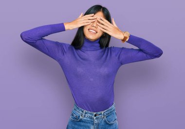 Güzel, genç Asyalı bir kadın, günlük kıyafetler giyip, elleri ile gözlerini kapatıyor, neşeli ve komik gülümsüyor. kör kavram. 