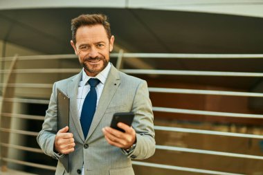 Şehirdeki akıllı telefondan gülümseyen orta yaşlı bir işadamı..