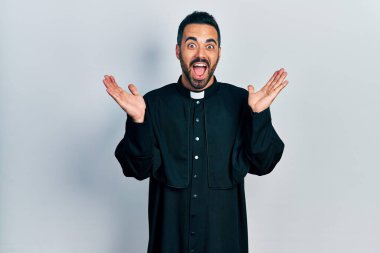 Sarışın, sakallı, katolik rahip cübbesi giyen yakışıklı, çılgın ve başarıyı kolları açık, gözleri açık ve heyecanlı bir şekilde kutlayan bir adam. Kazanan konsept 