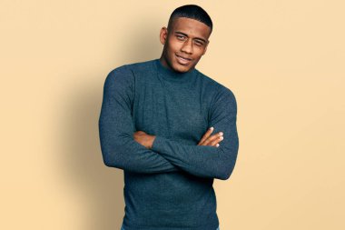 Genç siyah adam kollarını kavuşturup kameraya bakarken gülen mutlu bir yüz takınıyor. pozitif kişi. 