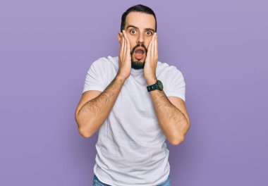 Sakallı, sıradan beyaz tişörtlü, korkmuş ve şok olmuş genç bir adam. 