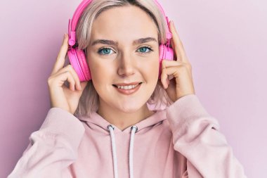 Müzik dinleyen, kulaklık takan, mutlu ve havalı bir gülümsemeyle gülümseyen genç sarışın kız. diş gösterme. 