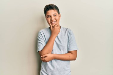 Gündelik gri tişört giyen genç İspanyol çocuk kameraya kollarını kavuşturup gülümseyen ve çenesini kaldıran kendinden emin bir şekilde bakıyor. Olumlu düşünmek. 