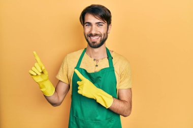 Temiz önlük ve eldiven giyen genç İspanyol adam gülümseyip kameraya bakıyor ve iki eliyle ve parmaklarıyla kenarı işaret ediyor.. 