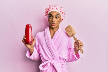 Duş başlığı takıp makyaj yapan İspanyol bir adam elinde sünger, şampuanından bihaber ve kafası karışık bir ifade takınıyor. şüphe kavramı. 