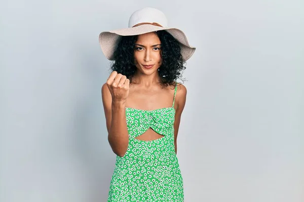 Young latin girl wearing summer hat angry and mad raising fist frustrated and furious while shouting with anger. rage and aggressive concept.