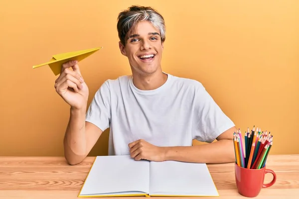 Młody Hiszpan Studiujący Trzymający Papierowy Samolot Siedzący Stole Wyglądający Pozytywnie — Zdjęcie stockowe