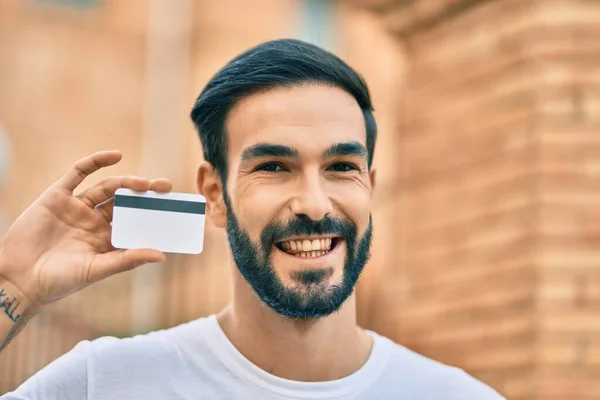 Joven Hispano Sonriendo Feliz Sosteniendo Tarjeta Crédito Ciudad —  Fotos de Stock