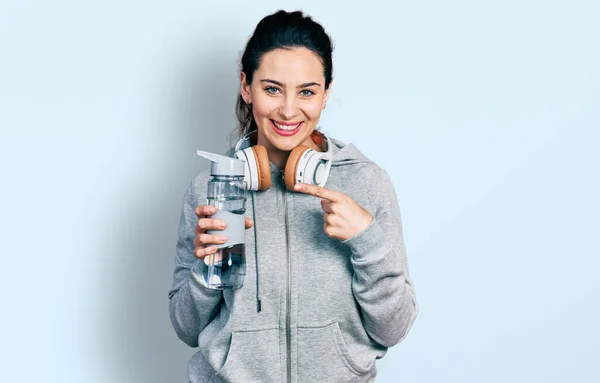 若いですヒスパニック女性身に着けていますスポーツウェア保持水ボトル使用ヘッドフォン笑顔幸せなポインティングで手と指 — ストック写真