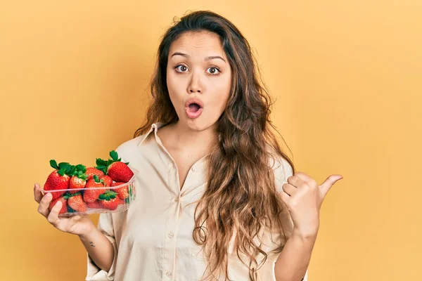 Joven Chica Hispana Sosteniendo Fresas Sorprendida Apuntando Con Dedo Mano — Foto de Stock