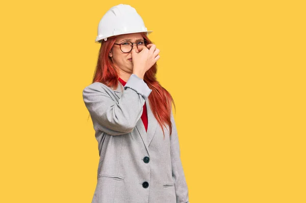 年轻的红头发女人戴着建筑师的硬礼帽 闻到一股难闻恶心的气味 用手指捂住鼻子屏住呼吸 — 图库照片