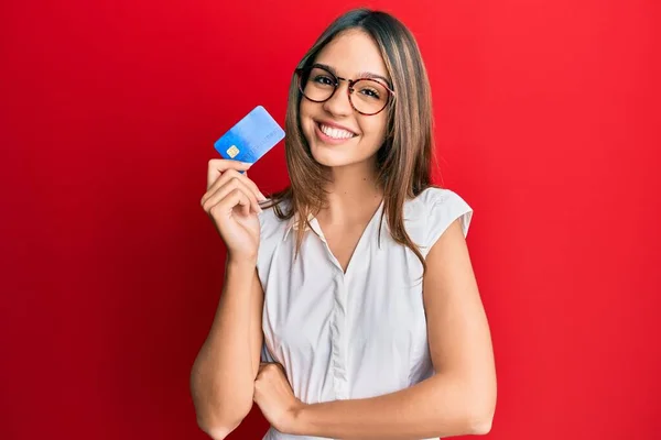 Młoda Brunetka Trzymająca Kartę Kredytową Uśmiechnięta Szczęśliwym Chłodnym Uśmiechem Twarzy — Zdjęcie stockowe