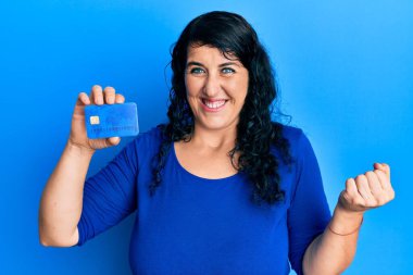 Artı, kredi kartı tutan esmer kadın gururla bağırıyor, zaferi kutluyor ve başarıyı kollarını kaldırarak kutluyor. 