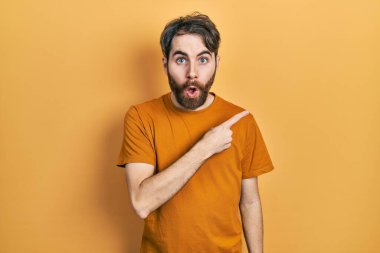 Sakallı, sıradan sarı tişörtlü, beyaz bir adam parmakları yanda, ağzı açık, şaşkın bir ifadeyle şaşırdı.. 