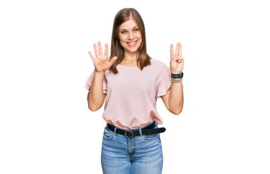 Güzel, beyaz bir kadın, günlük kıyafetler giyip 8 numaralı parmaklarıyla işaret ederken kendine güvenen ve mutlu bir şekilde gülümsüyor.. 