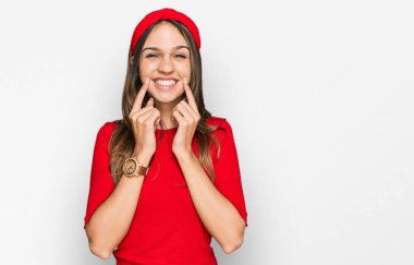 Genç esmer kadın gündelik kıyafetler giyip ağzı açık gülümsüyor, parmakları işaret ediyor ve neşeli bir gülümseme sergiliyor. 