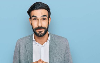 İş kıyafetleri giyen genç İspanyol adam ellerini birleştirip gülümseyerek gevşemiş ve neşeliydi. Başarı ve iyimserlik 