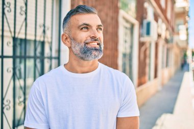 Orta yaşlı, kır saçlı, gülümseyen bir adam şehirde mutlu bir şekilde duruyor..