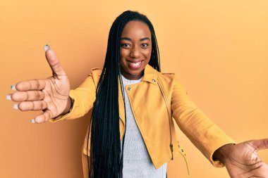 Sıradan bir ceket giyen genç Afro-Amerikan kadın kameraya sarılıp gülümseyerek bakıyor. Mutluluğu kucaklayan neşeli bir ifade.. 