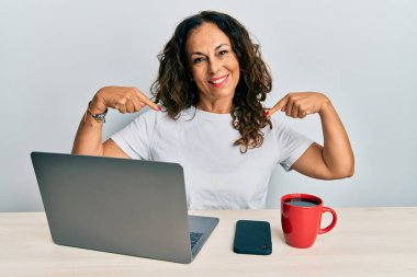 Ofiste çalışan orta yaşlı güzel bir kadın bilgisayar kullanıyor. Kendine güveni tam görünüyor. Kendini gururlu ve mutlu gösteriyor.. 