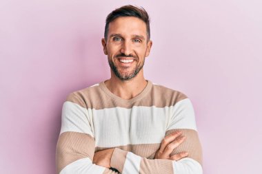 Sakallı, sıradan giyinen, mutlu yüzlü, kollarını kavuşturup kameraya bakan yakışıklı bir adam. pozitif kişi. 