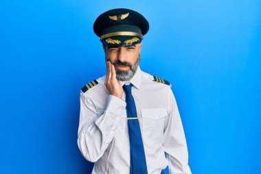Sakallı, gri saçlı, uçak pilotu üniforması giyen, diş ağrısı ya da diş hastalığından dolayı ağızlarına acı dolu bir ifadeyle dokunan orta yaşlı bir adam. dişçi 
