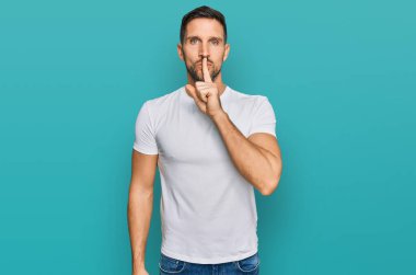 Sakallı, sıradan beyaz tişörtlü, dudakları parmaklı yakışıklı bir adam sessiz olmak istiyor. sessizlik ve gizli konsept. 