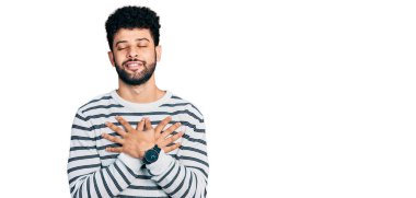 Sakallı, sıradan çizgili süveter giyen, elleri göğsünde, gözleri kapalı ve yüzünde minnet ifadesi olan genç bir Arap. sağlık kavramı. 