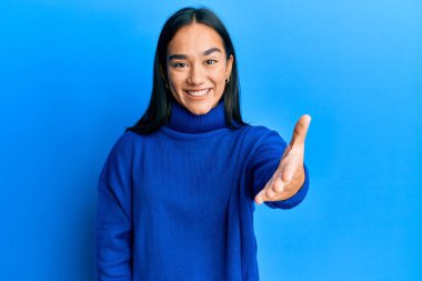 Sıradan bir kazak giyen Asyalı genç bir kadın selamlama ve hoş geldin demek için dostça bir şekilde tokalaşıyor. başarılı iş. 